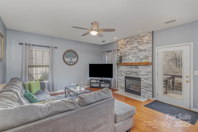 living room featuring a fireplace, visible vents, ceiling fan, wood finished floors, and baseboards