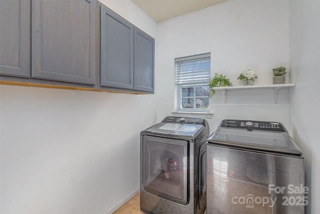 clothes washing area featuring cabinet space, light tile patterned floors, and washer and clothes dryer