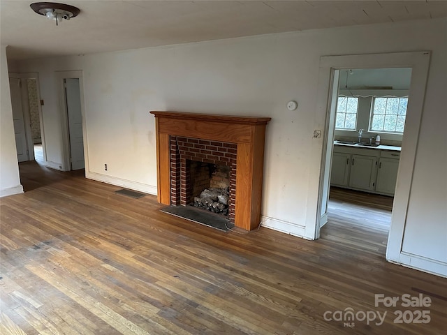 unfurnished living room featuring dark wood-type flooring, sink, and a fireplace