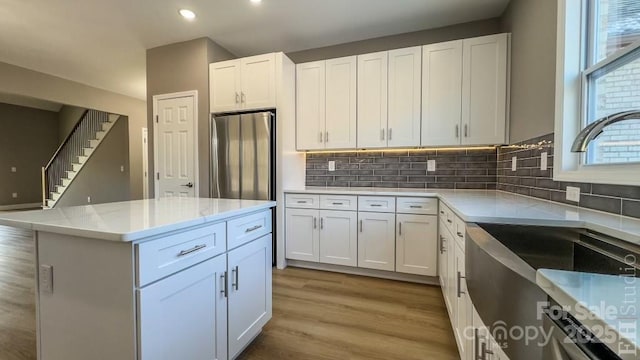 kitchen with sink, white cabinetry, tasteful backsplash, light hardwood / wood-style flooring, and stainless steel fridge