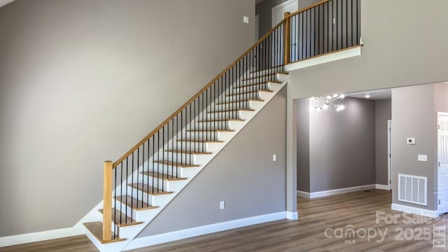 stairs with hardwood / wood-style flooring, a chandelier, and a high ceiling