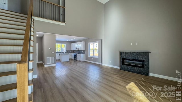 unfurnished living room with hardwood / wood-style flooring, a tiled fireplace, and a high ceiling