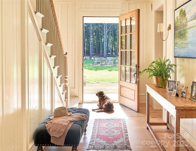 doorway featuring light wood-style flooring, stairs, and wooden walls