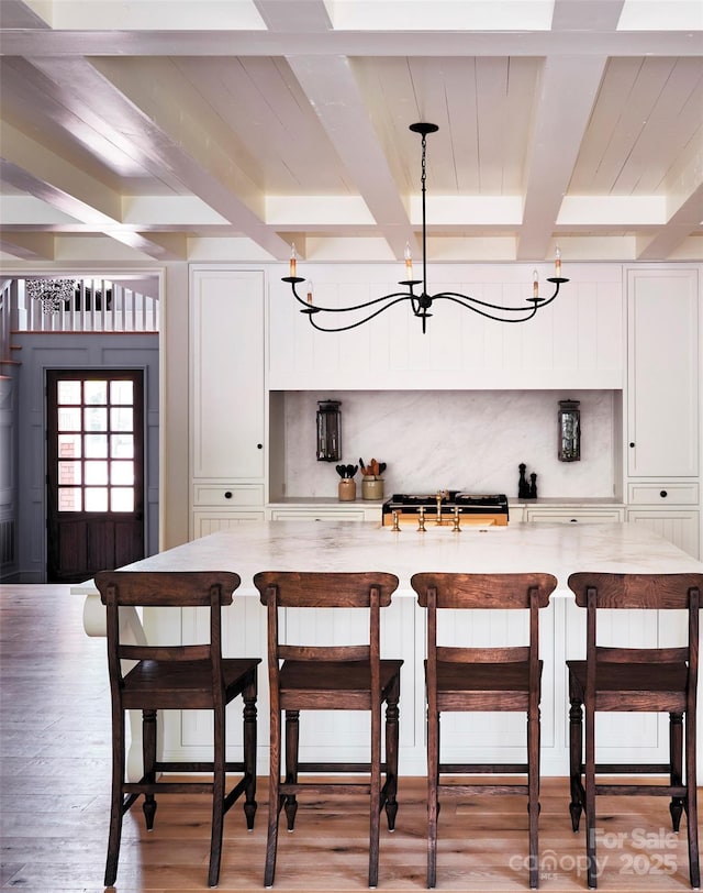 kitchen with an inviting chandelier, beam ceiling, a breakfast bar area, white cabinetry, and light wood-style floors