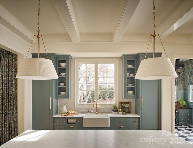 kitchen featuring hanging light fixtures, beam ceiling, glass insert cabinets, a sink, and light countertops