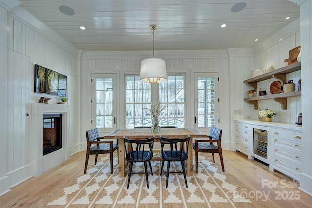 dining room featuring recessed lighting, beverage cooler, light wood-type flooring, wood ceiling, and a glass covered fireplace