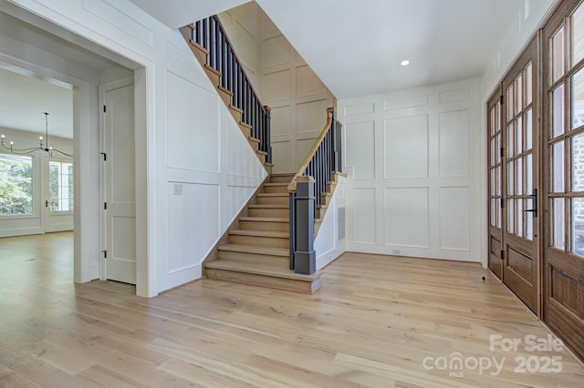 entrance foyer featuring a decorative wall, a notable chandelier, light wood-style floors, and stairway