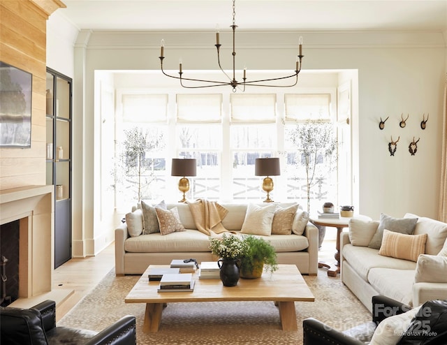 living room with a fireplace, light wood-type flooring, a notable chandelier, and ornamental molding