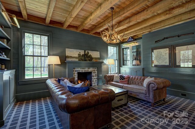 living room with wood walls, a stone fireplace, an inviting chandelier, beamed ceiling, and wood ceiling