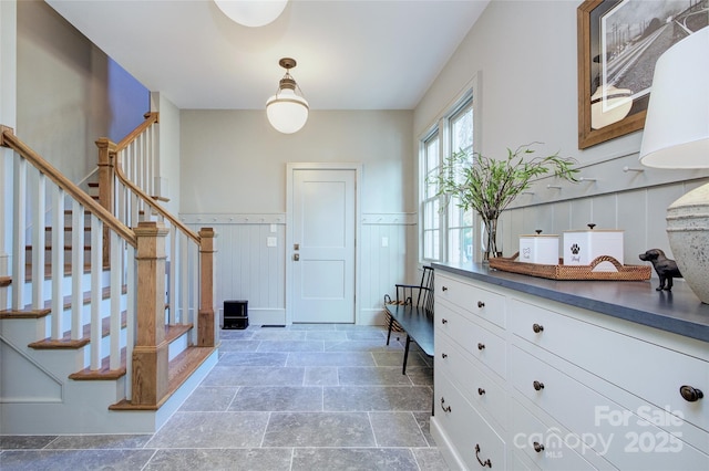 foyer entrance featuring stairway, a wainscoted wall, and stone finish flooring