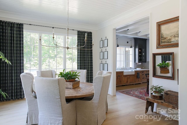 dining room featuring light wood-style flooring, a healthy amount of sunlight, a notable chandelier, and crown molding