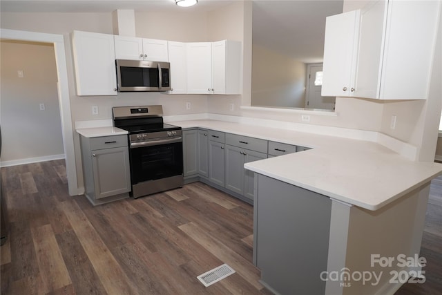 kitchen with gray cabinets, white cabinets, dark hardwood / wood-style flooring, kitchen peninsula, and stainless steel appliances