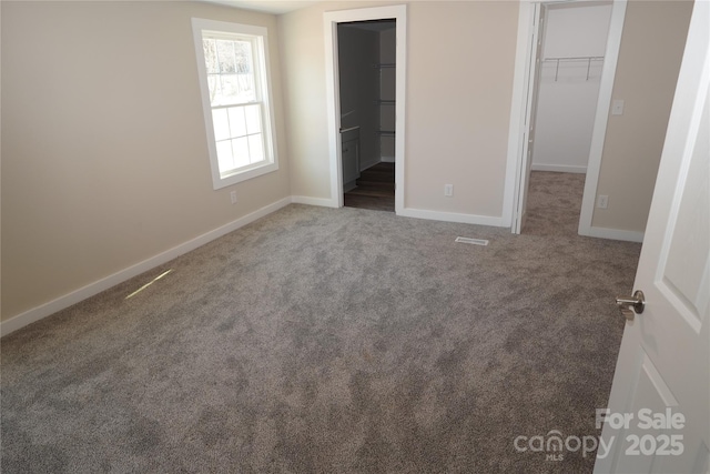 unfurnished bedroom featuring dark colored carpet, a spacious closet, connected bathroom, and a closet