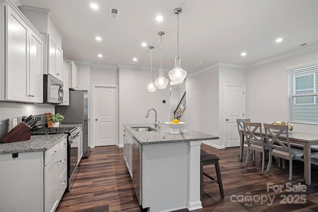 kitchen with sink, white cabinetry, pendant lighting, stainless steel appliances, and an island with sink