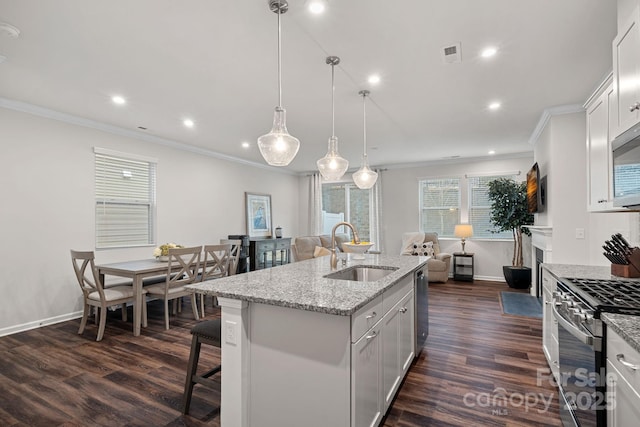 kitchen with stainless steel appliances, white cabinets, pendant lighting, sink, and a kitchen island with sink