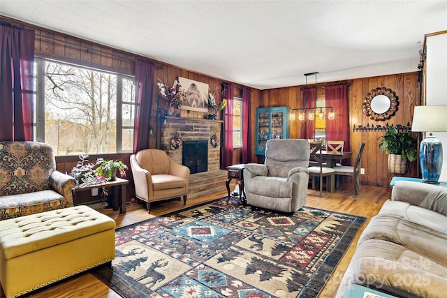 living room with hardwood / wood-style floors, a stone fireplace, wooden walls, and a textured ceiling