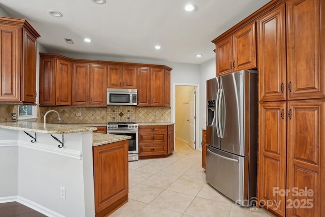 kitchen featuring appliances with stainless steel finishes, a breakfast bar, tasteful backsplash, light stone counters, and kitchen peninsula