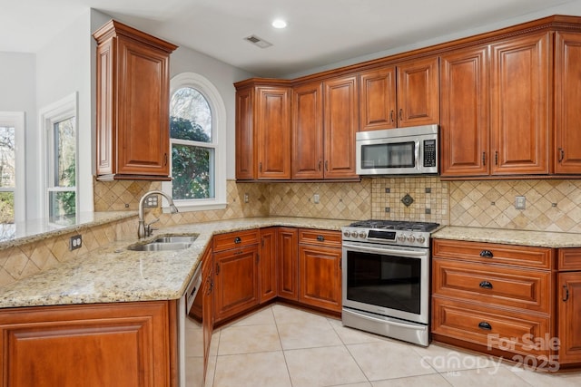 kitchen with light tile patterned flooring, appliances with stainless steel finishes, sink, light stone counters, and kitchen peninsula