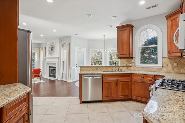 kitchen with light stone counters, sink, hanging light fixtures, and appliances with stainless steel finishes