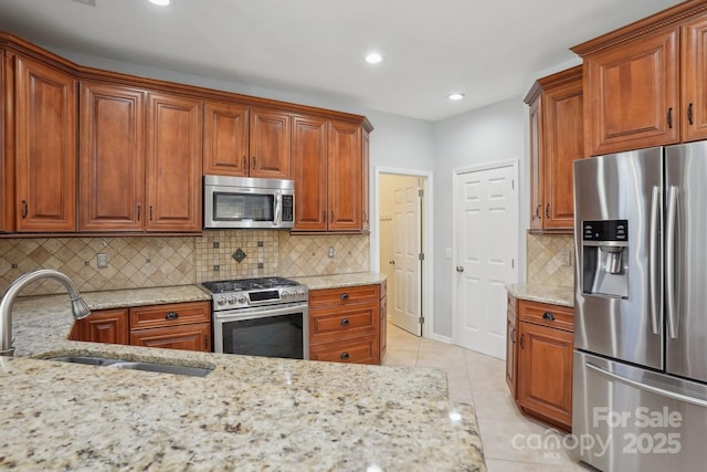 kitchen featuring sink, light tile patterned floors, stainless steel appliances, light stone countertops, and decorative backsplash