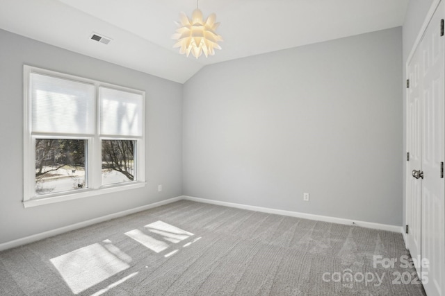 empty room featuring lofted ceiling, light carpet, and a chandelier