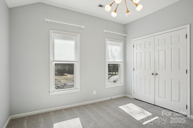 unfurnished bedroom with a closet, lofted ceiling, light carpet, and a notable chandelier