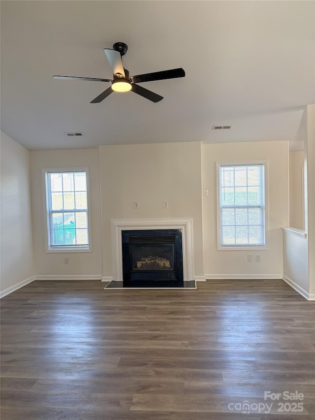 unfurnished living room featuring dark wood-type flooring, plenty of natural light, visible vents, and a fireplace