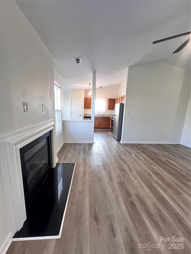 unfurnished living room with lofted ceiling, visible vents, baseboards, light wood-type flooring, and a glass covered fireplace