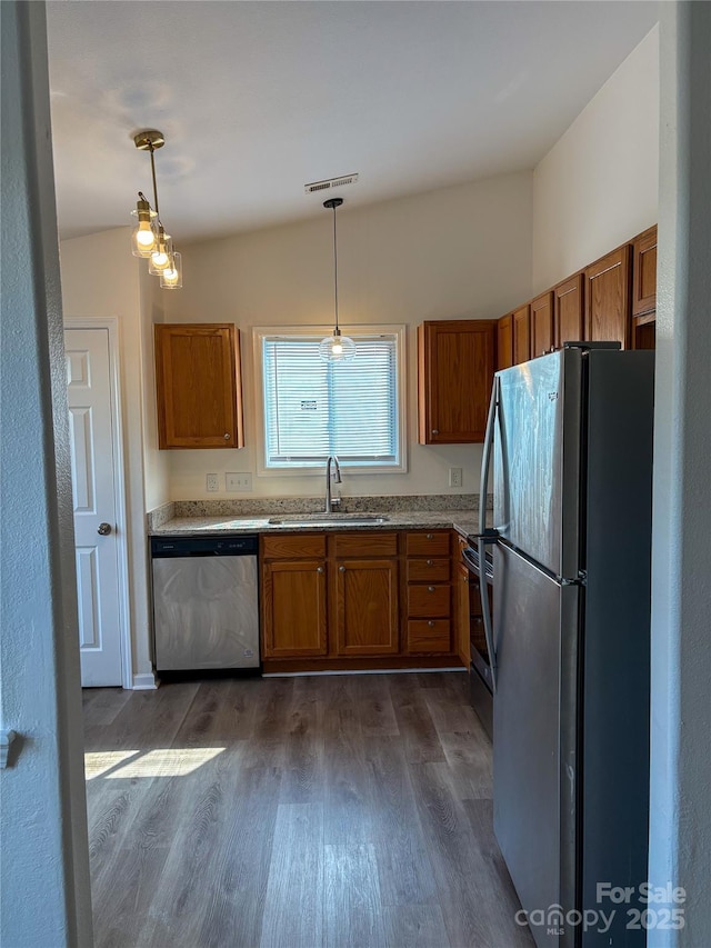 kitchen with brown cabinetry, pendant lighting, stainless steel appliances, and a sink