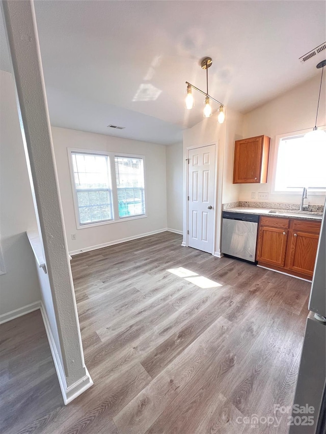 kitchen featuring hanging light fixtures, stainless steel dishwasher, brown cabinetry, and a sink