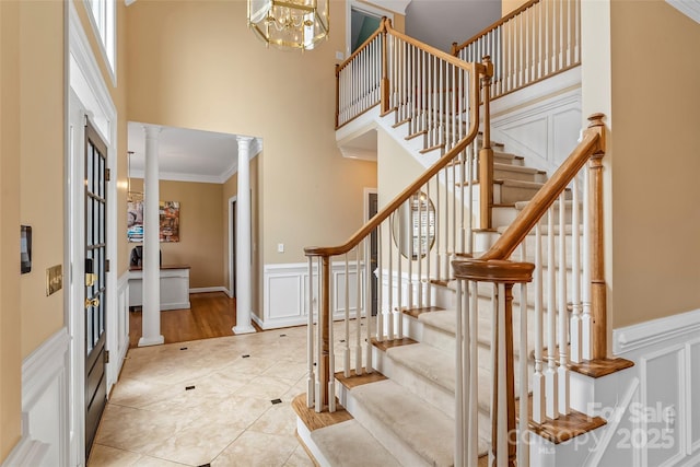 entrance foyer with ornate columns, a towering ceiling, ornamental molding, light tile patterned floors, and an inviting chandelier