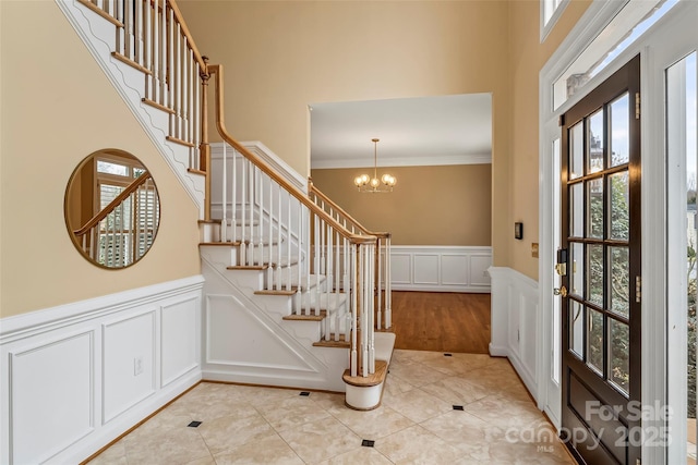 tiled foyer entrance featuring ornamental molding, a high ceiling, and a notable chandelier