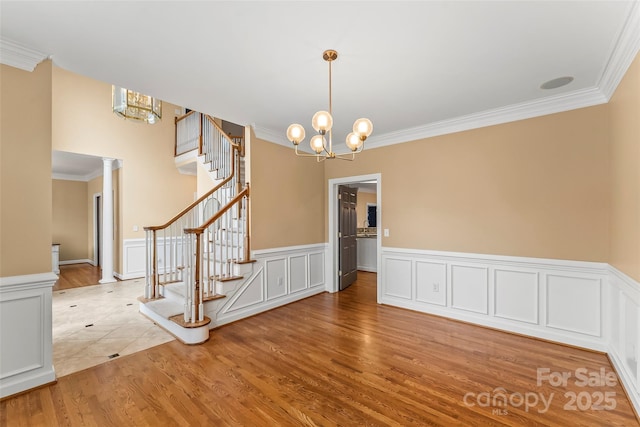 unfurnished dining area featuring ornate columns, crown molding, an inviting chandelier, and light hardwood / wood-style flooring