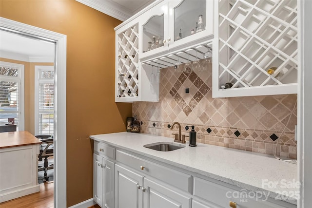 kitchen featuring sink, tasteful backsplash, light stone counters, ornamental molding, and white cabinets