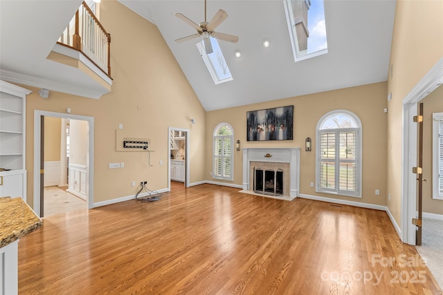 unfurnished living room featuring a tiled fireplace, a skylight, light hardwood / wood-style floors, and ceiling fan