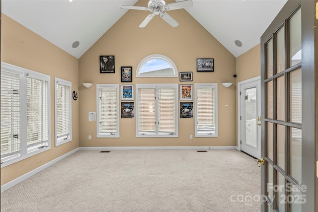 empty room with plenty of natural light, light colored carpet, and high vaulted ceiling