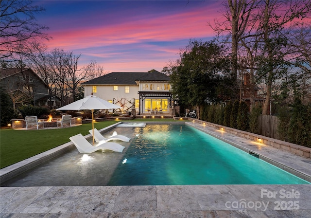 pool at dusk featuring a yard, a pergola, a patio area, and a fire pit