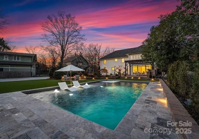 pool at dusk with pool water feature, a pergola, a patio area, and a lawn