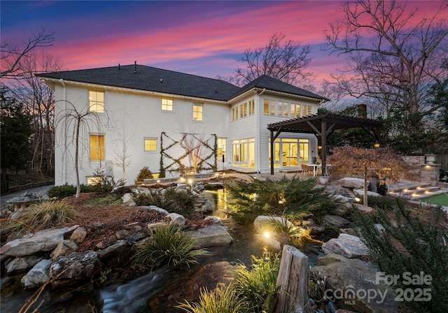 back house at dusk featuring a pergola