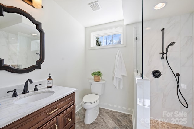 bathroom with a tile shower, vanity, and toilet