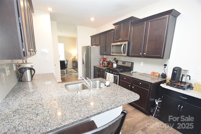 kitchen featuring dark brown cabinetry, sink, light hardwood / wood-style flooring, appliances with stainless steel finishes, and light stone countertops