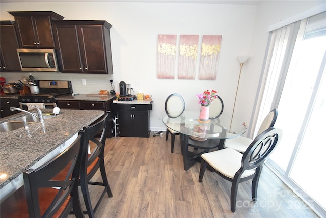 kitchen featuring sink, dark stone countertops, dark brown cabinets, stainless steel appliances, and light hardwood / wood-style floors