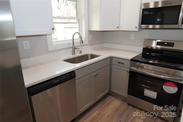 kitchen featuring sink, light hardwood / wood-style flooring, gray cabinets, stainless steel appliances, and white cabinets