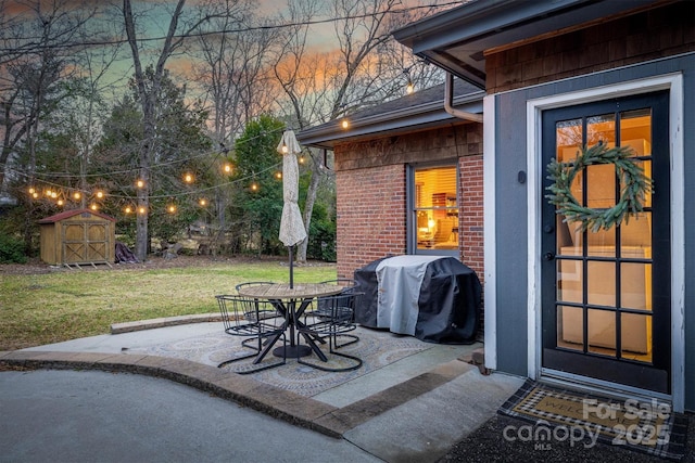 patio terrace at dusk featuring a shed, grilling area, and a lawn