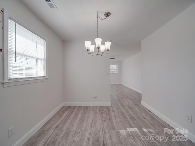 spare room with plenty of natural light, a chandelier, and light hardwood / wood-style flooring