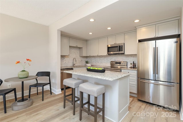 kitchen with a kitchen island, appliances with stainless steel finishes, tasteful backsplash, light hardwood / wood-style floors, and light stone countertops