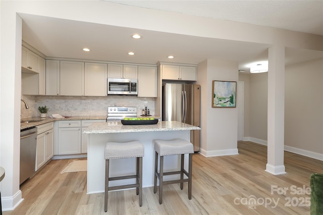 kitchen with a kitchen island, appliances with stainless steel finishes, sink, decorative backsplash, and light stone countertops