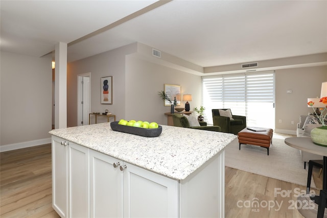 kitchen with white cabinetry, light stone counters, a kitchen island, and light wood-type flooring