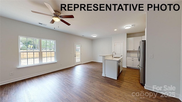 kitchen with sink, dark wood-type flooring, appliances with stainless steel finishes, white cabinetry, and a kitchen island with sink