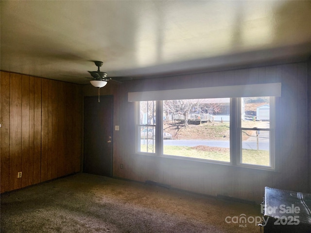 unfurnished dining area featuring ceiling fan, carpet floors, and wooden walls